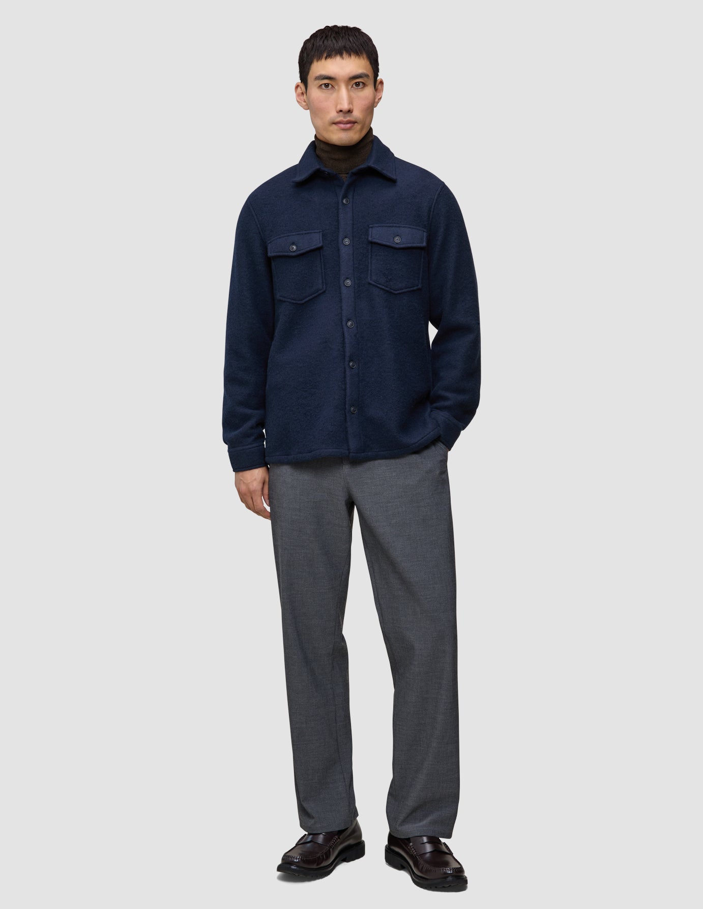 En person, der bærer en dobbeltlags uldskjorte i mørk marineblå i regular-pasform over en mørk sweater, grå bukser og mørke loafers.